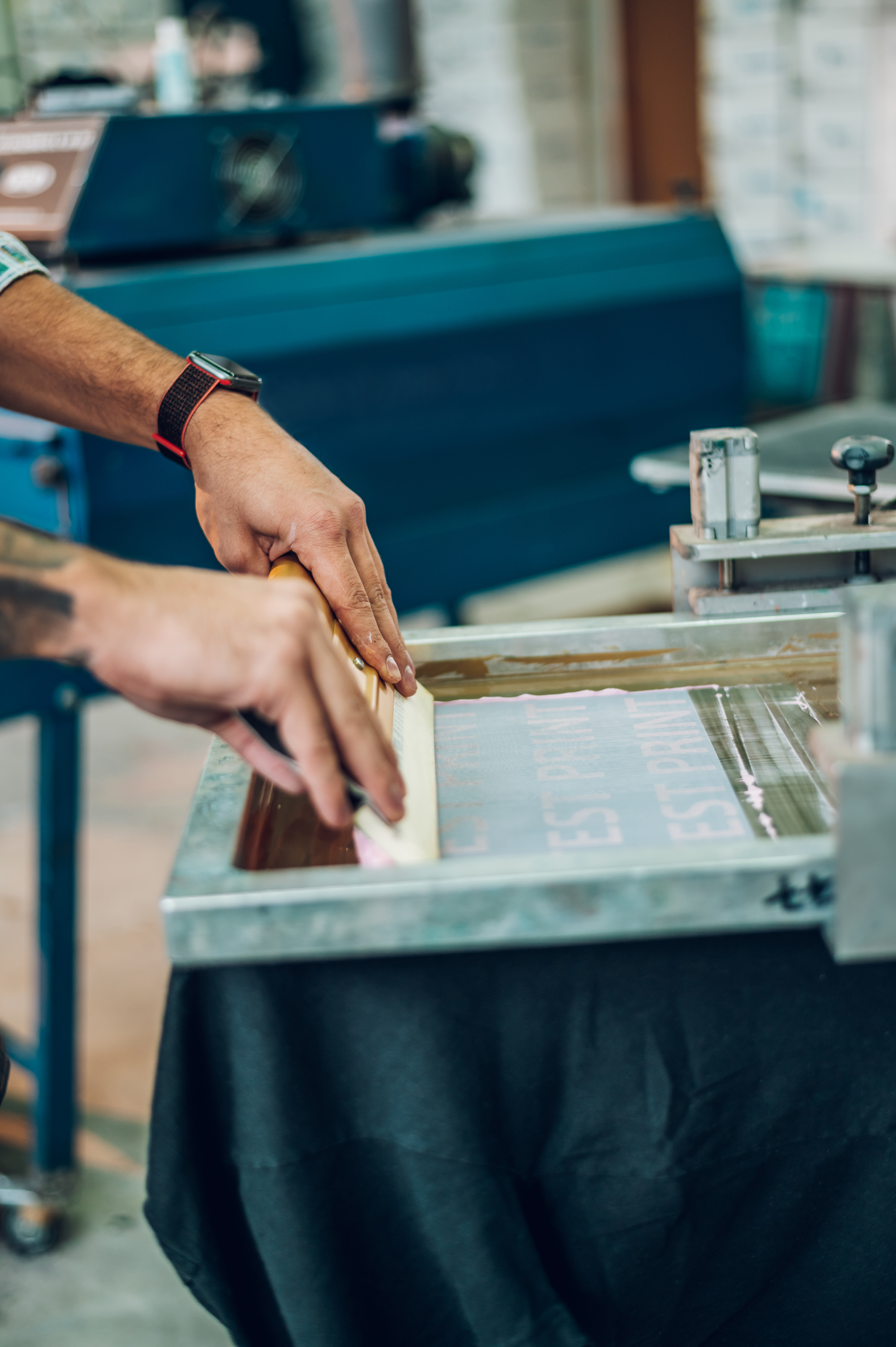 Male worker pressing ink on frame while using the printing machine in a workshop